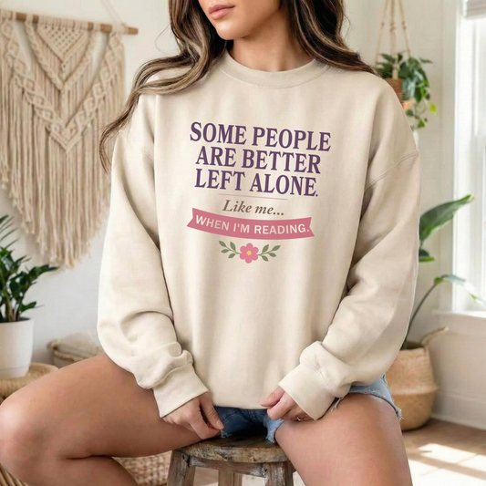 A woman wearing a cream-colored crewneck sweatshirt with a purple and pink graphic text that reads 'SOME PEOPLE ARE BETTER LEFT ALONE. Like me.