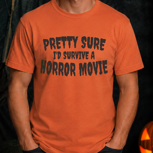 An orange crewneck t-shirt with the text 'PRETTY SURE I'D SURVIVE A HORROR MOVIE' printed in a distressed black font across the chest, worn by a model.