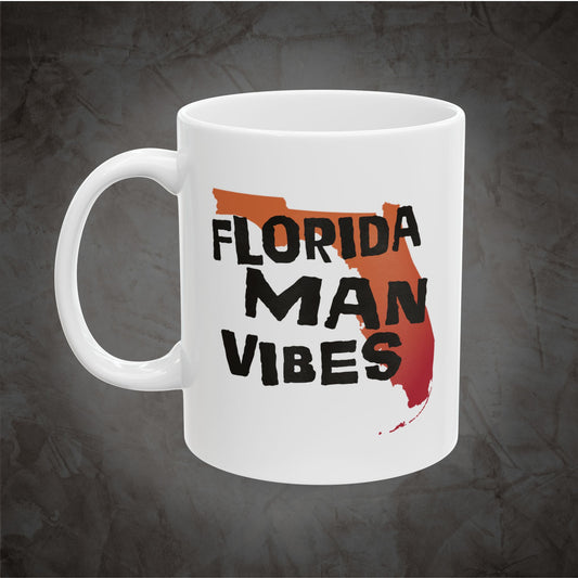 A white ceramic mug featuring a graphic design with the text 'FLORIDA MAN VIBES' in black over a red and orange Florida state outline, set against a dark textured gray background.