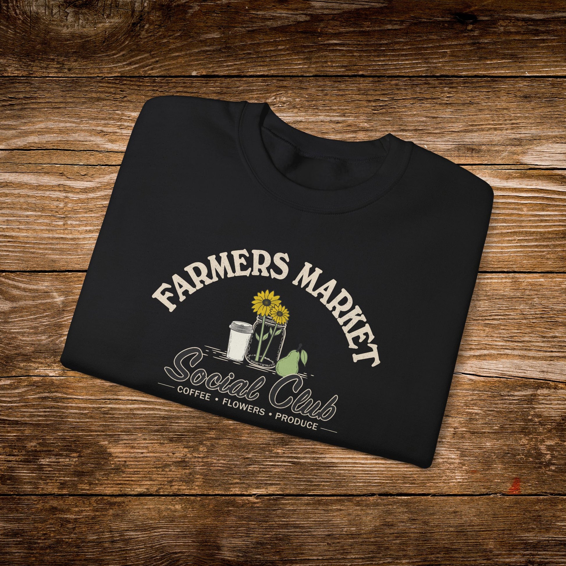 A black folded t-shirt with a 'Farmers Market Social Club' graphic, displayed on a rustic wooden background.