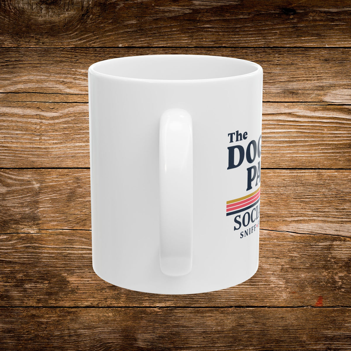 A white ceramic coffee mug with a handle, featuring a printed graphic that reads 'The Dog Patsy Social Club' in navy blue text with a retro striped accent, set against a rustic brown wooden background.