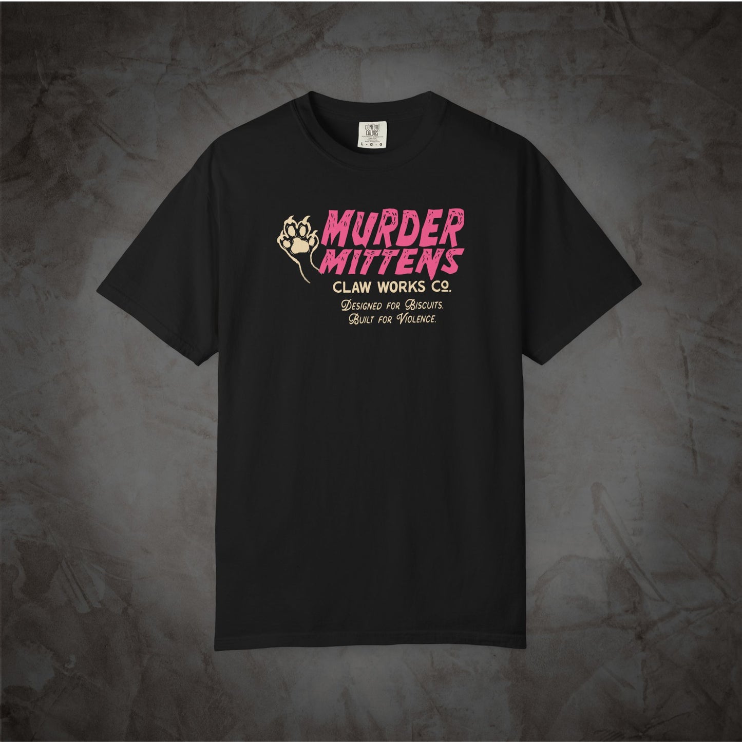 A black short-sleeve t-shirt with a graphic print on the chest reading 'MURDER MITTENS CLAW WORKS CO.' in pink and beige, displayed against a textured dark gray background.