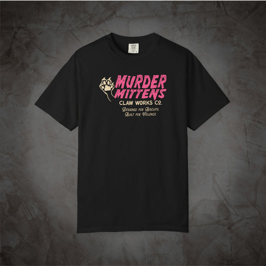 A black short-sleeve t-shirt with a graphic print on the chest reading 'MURDER MITTENS CLAW WORKS CO.' in pink and beige, displayed against a textured dark gray background.