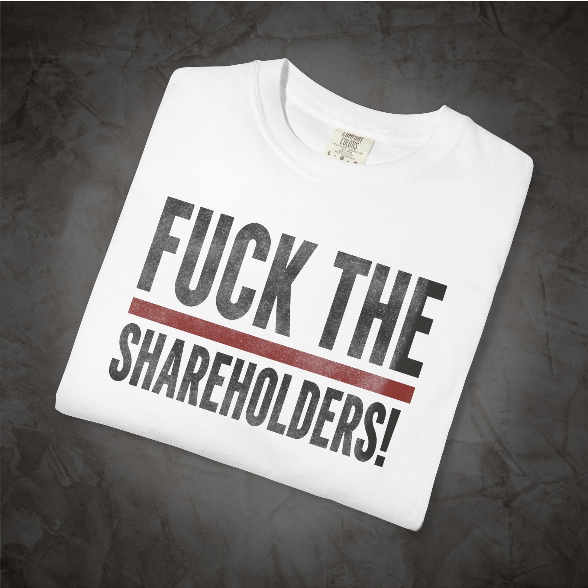 A white crewneck t-shirt with the text 'FUCK THE SHAREHOLDERS!' printed in black, separated by a thick red horizontal line, displayed on a dark textured background.