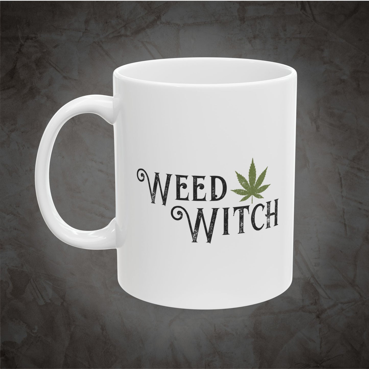 A white ceramic mug with the words 'WEED WITCH' printed in a dark gothic font, accompanied by a green cannabis leaf graphic, set against a dark textured gray background.