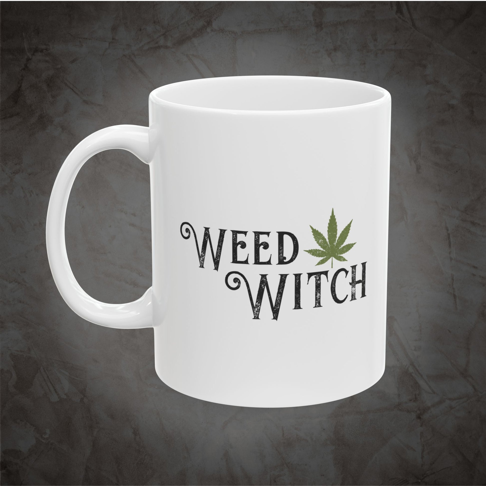 A white ceramic mug with the words 'WEED WITCH' printed in a dark gothic font, accompanied by a green cannabis leaf graphic, set against a dark textured gray background.
