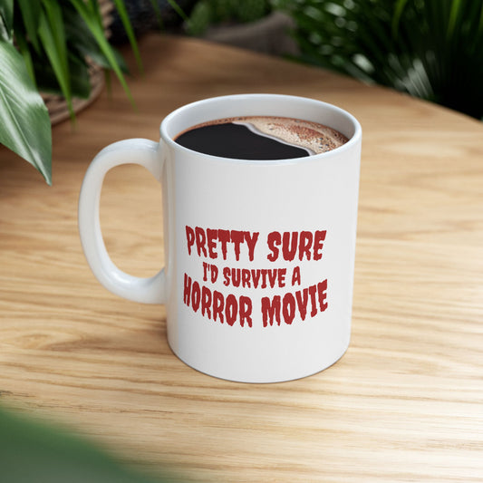 A white ceramic coffee mug with red text reading 'PRETTY SURE I'D SURVIVE A HORROR MOVIE' sits on a light wood table with green plants blurred in the background.