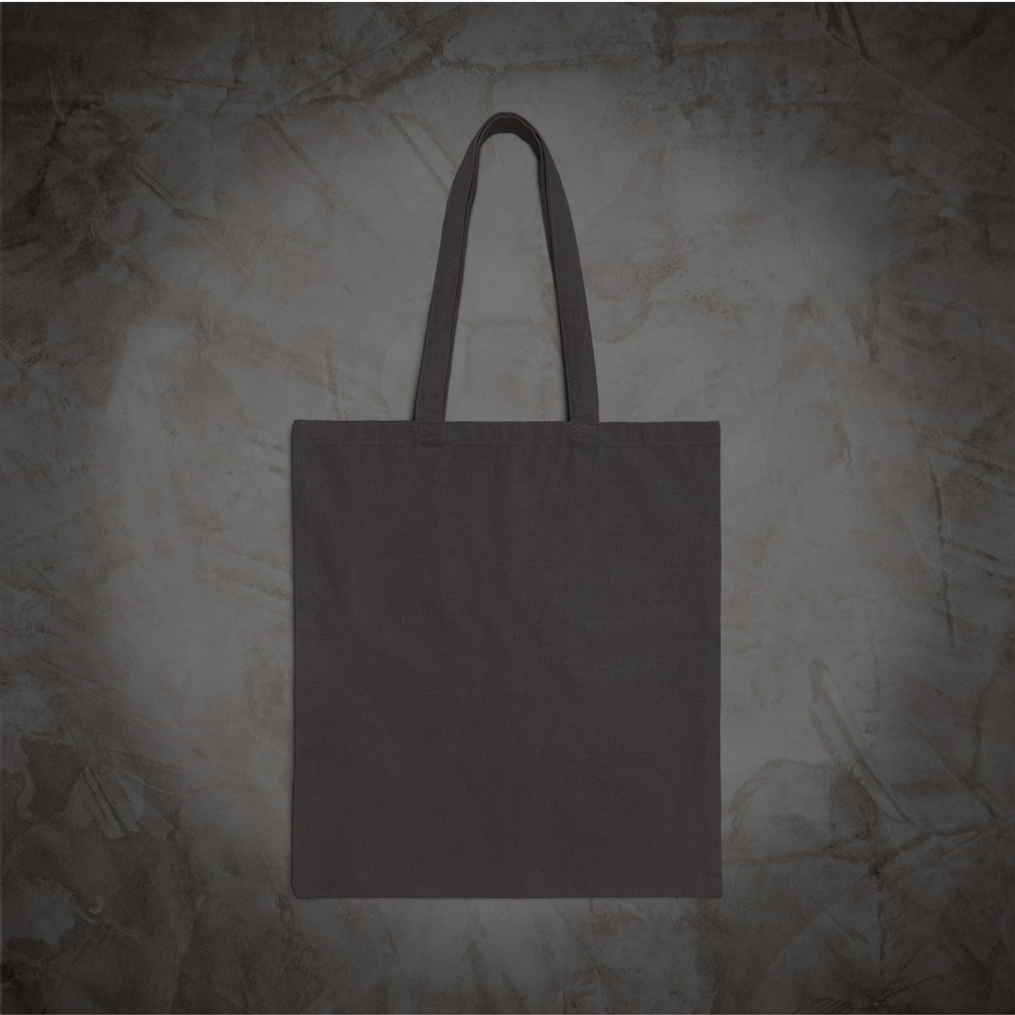 A plain dark gray canvas tote bag with two handles, centered against a textured gray background.