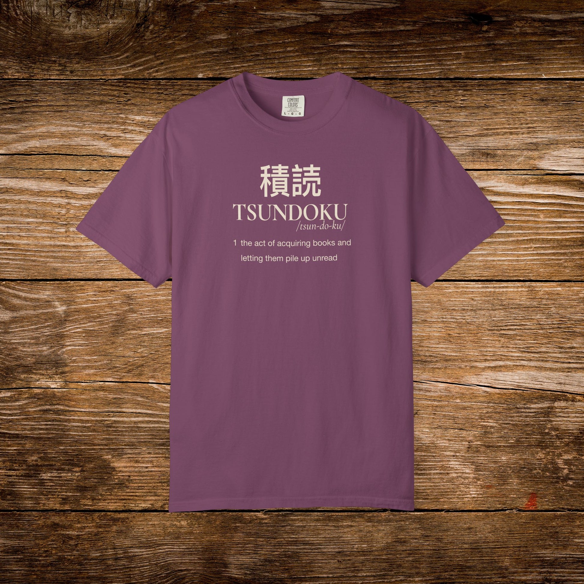 Tsundoku dictionary definition printed on a berry Comfort Colors T-shirt with minimalist vintage typography.