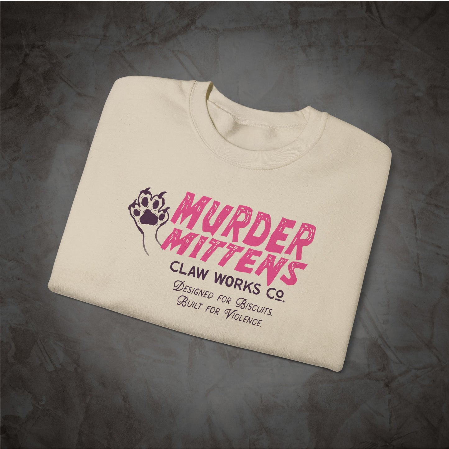 An off-white crewneck t-shirt with a pink and black graphic print reading 'MURDER MITTENS CLAW WORKS CO. DESIGNED FOR BISCUITS.
