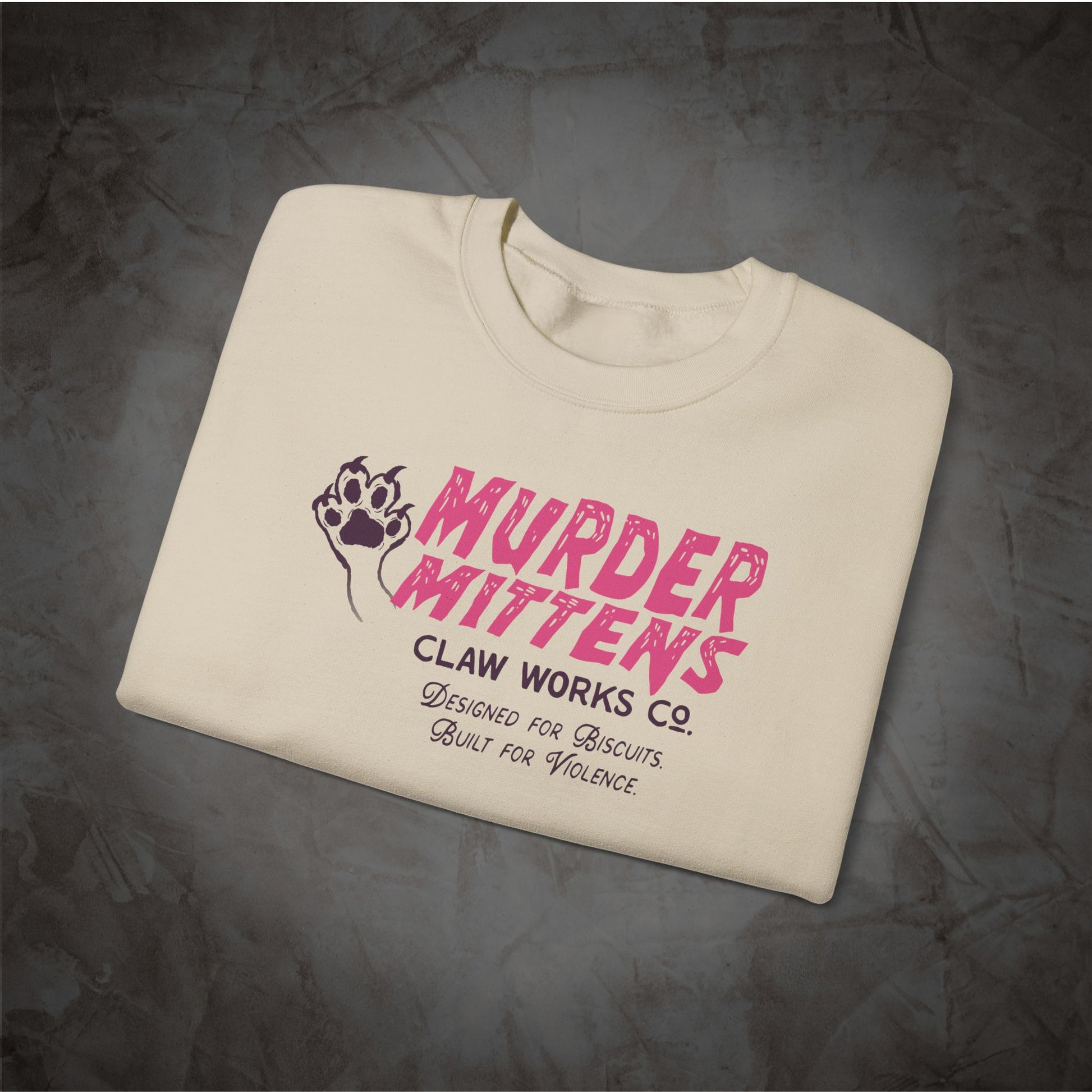 An off-white crewneck t-shirt with a pink and black graphic print reading 'MURDER MITTENS CLAW WORKS CO. DESIGNED FOR BISCUITS.
