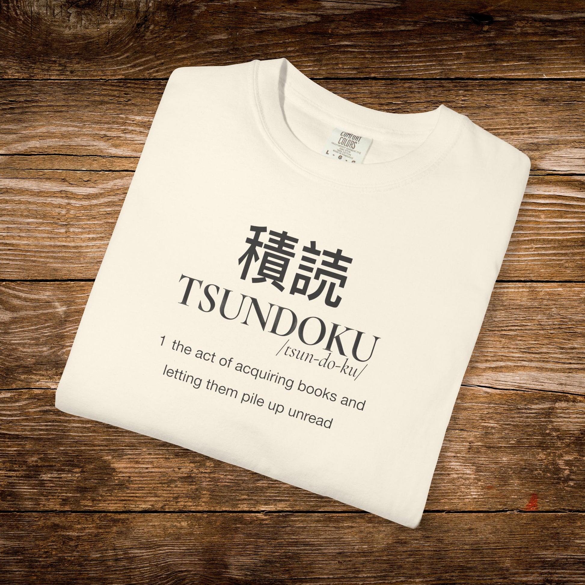 Folded ivory Comfort Colors T-shirt featuring the Tsundoku dictionary definition design.