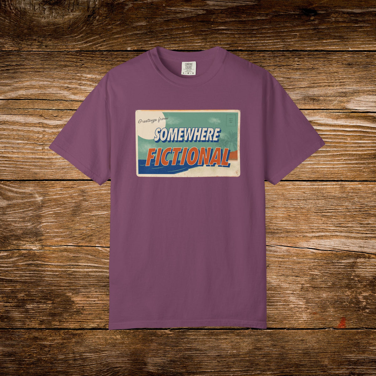 Berry Comfort Colors t-shirt with a colorful retro “Greetings from Somewhere Fictional” postcard illustration.