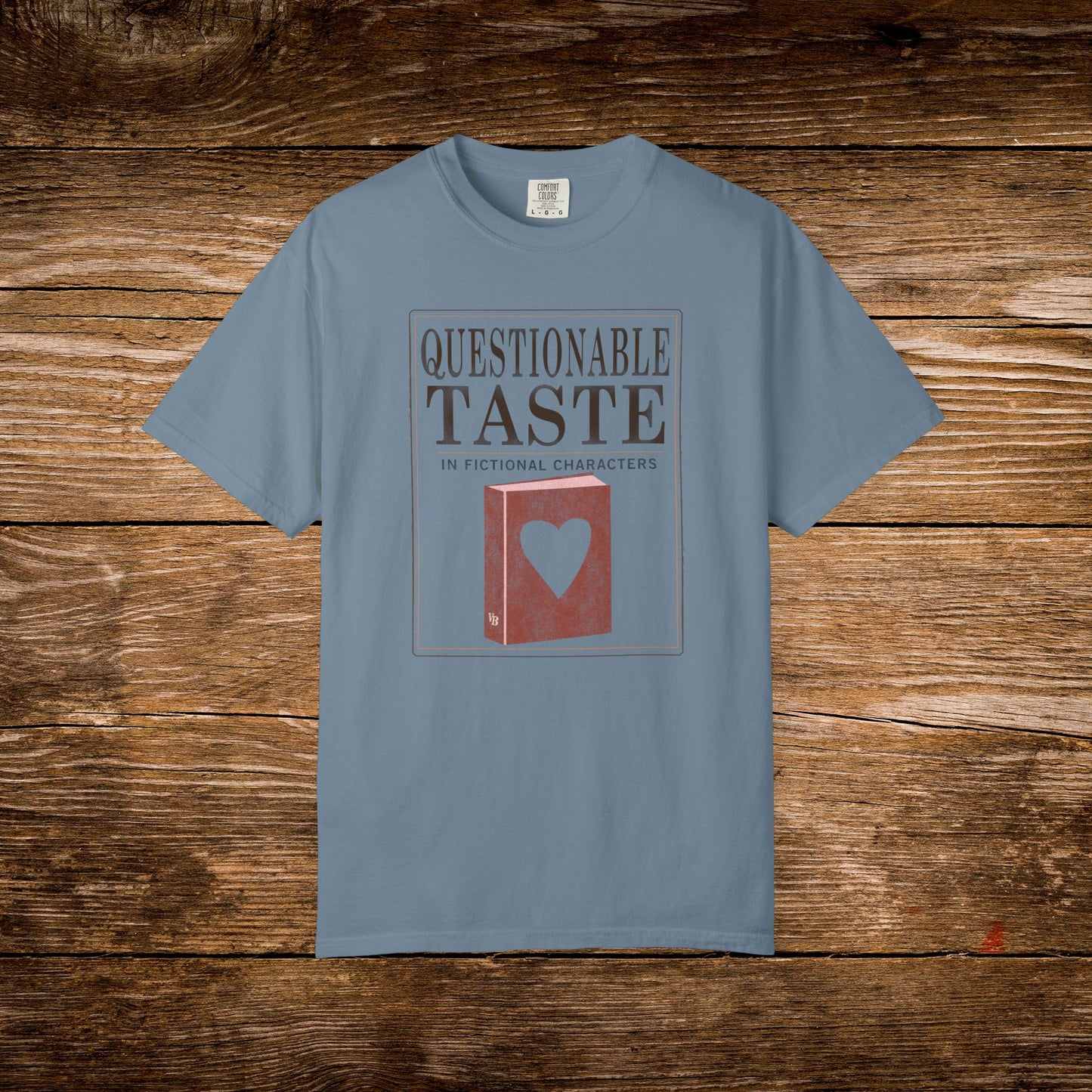 Blue t-shirt with 'Questionable Taste' graphic on a wooden surface