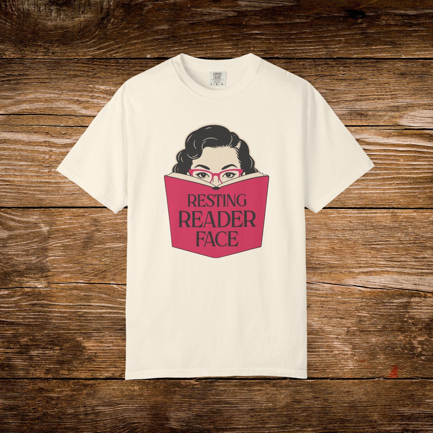 Ivory Resting Reader Face graphic t-shirt shown on a wooden background.