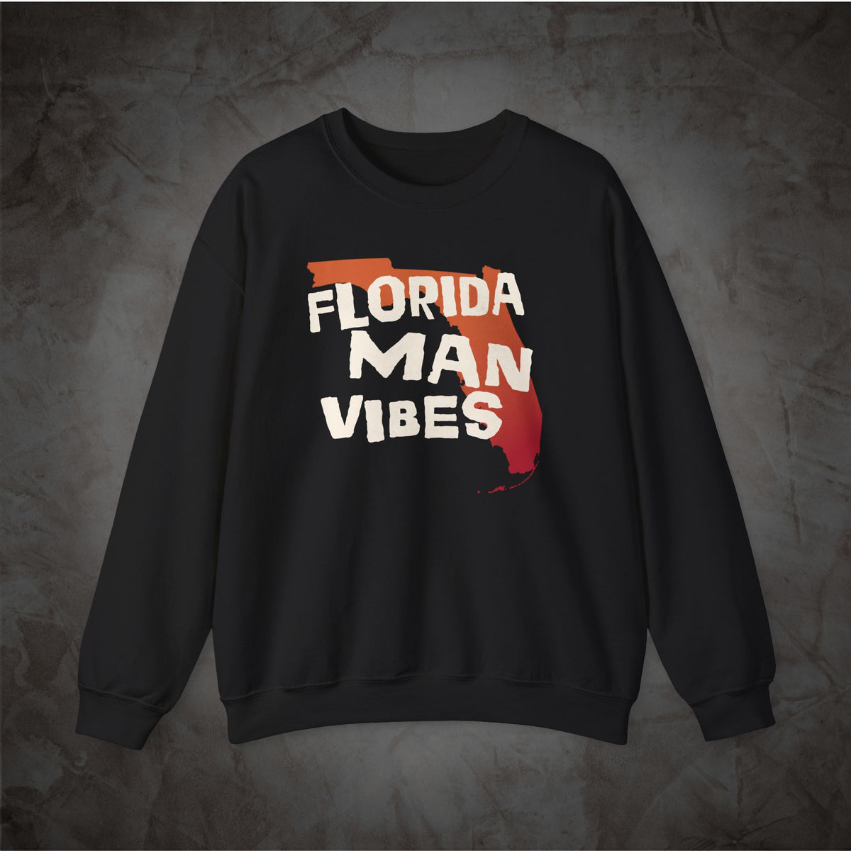 A black crewneck sweatshirt featuring a graphic print on the front with the words 'FLORIDA MAN VIBES' in white over a red and orange Florida state outline, displayed against a textured gray background.
