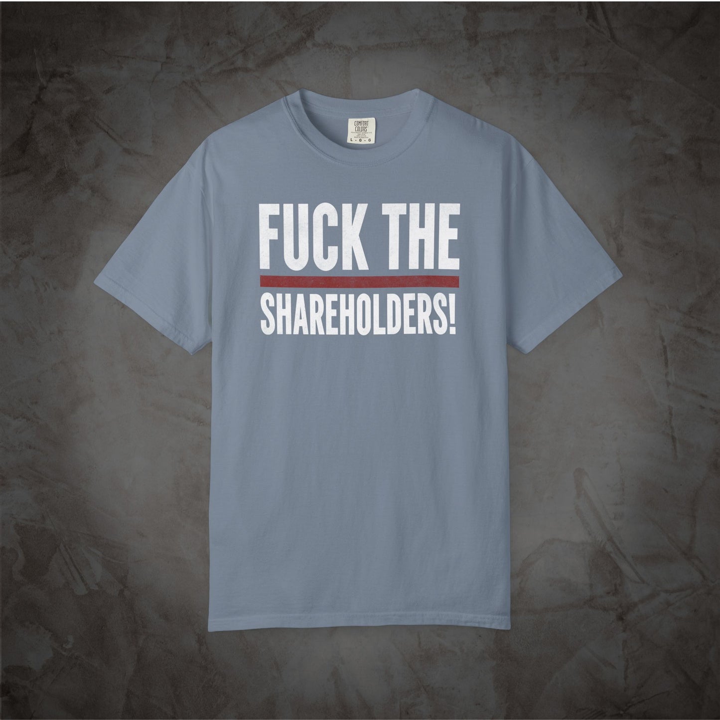 A light blue crewneck t-shirt with the text 'FUCK THE SHAREHOLDERS!' printed in white across the chest, separated by a thin red horizontal line, displayed against a textured gray background.