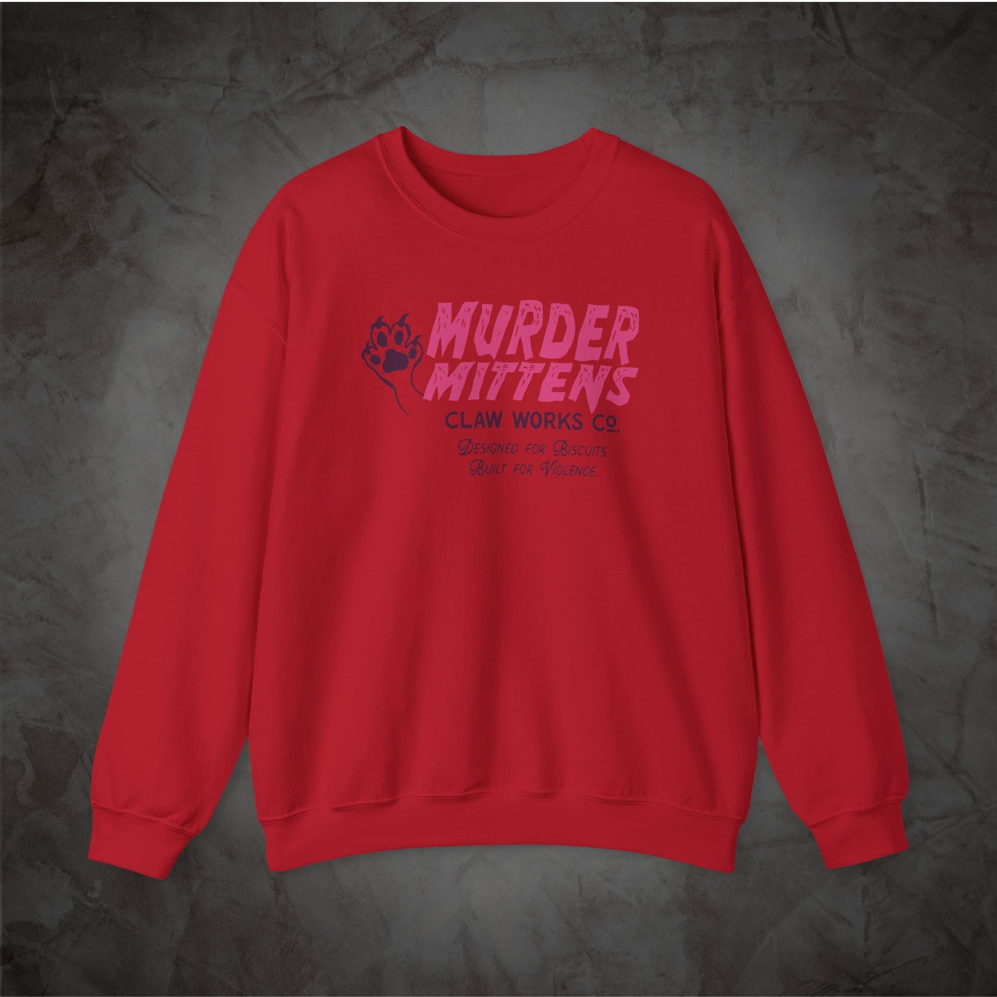 A red crewneck sweatshirt with a pink and dark blue graphic on the chest reading 'MURDER MITTENS CLAW WORKS CO' with a paw print, displayed on a dark textured background.
