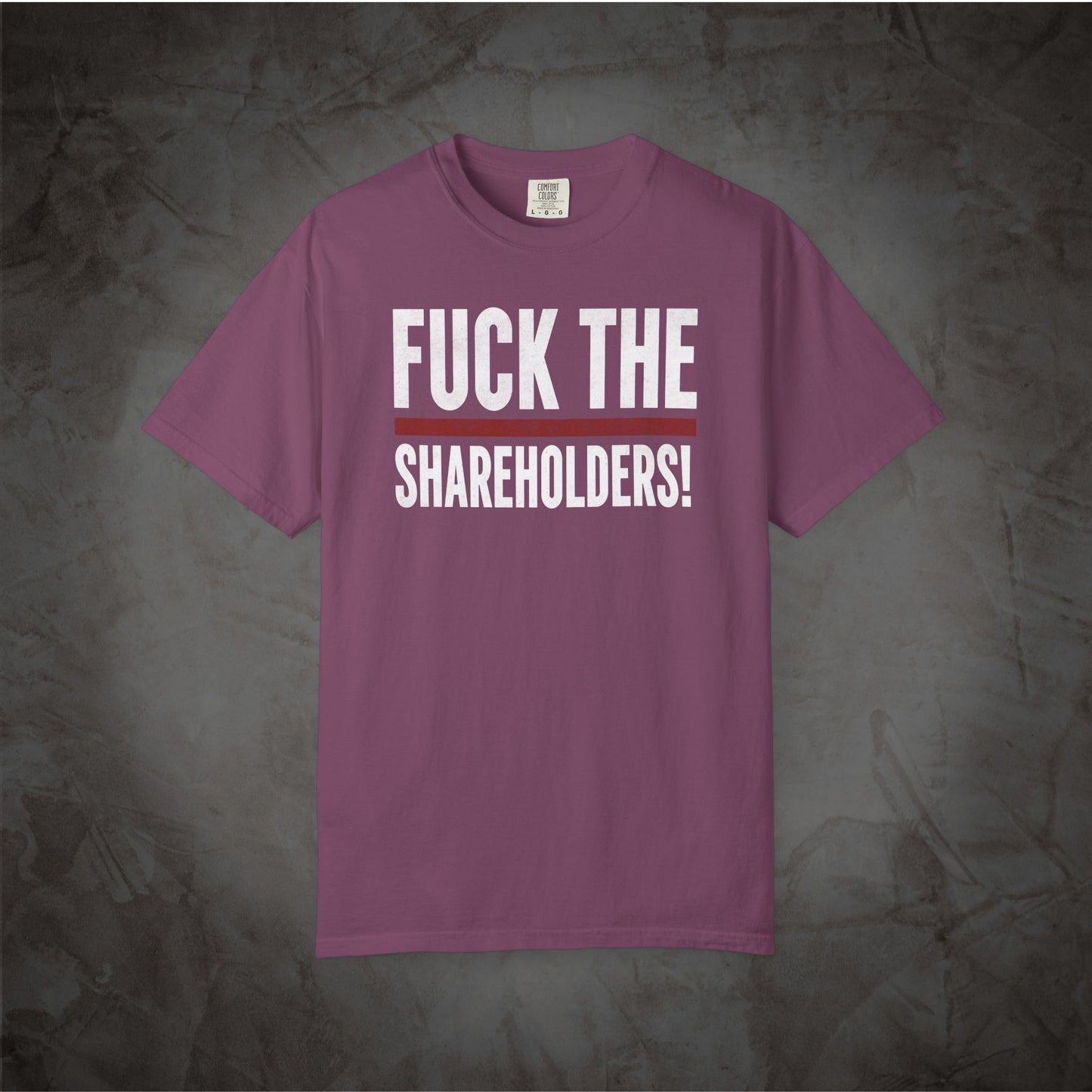 A mauve purple short-sleeve t-shirt with bold white text reading 'FUCK THE SHAREHOLDERS!' on the front, displayed flat against a textured dark gray background.