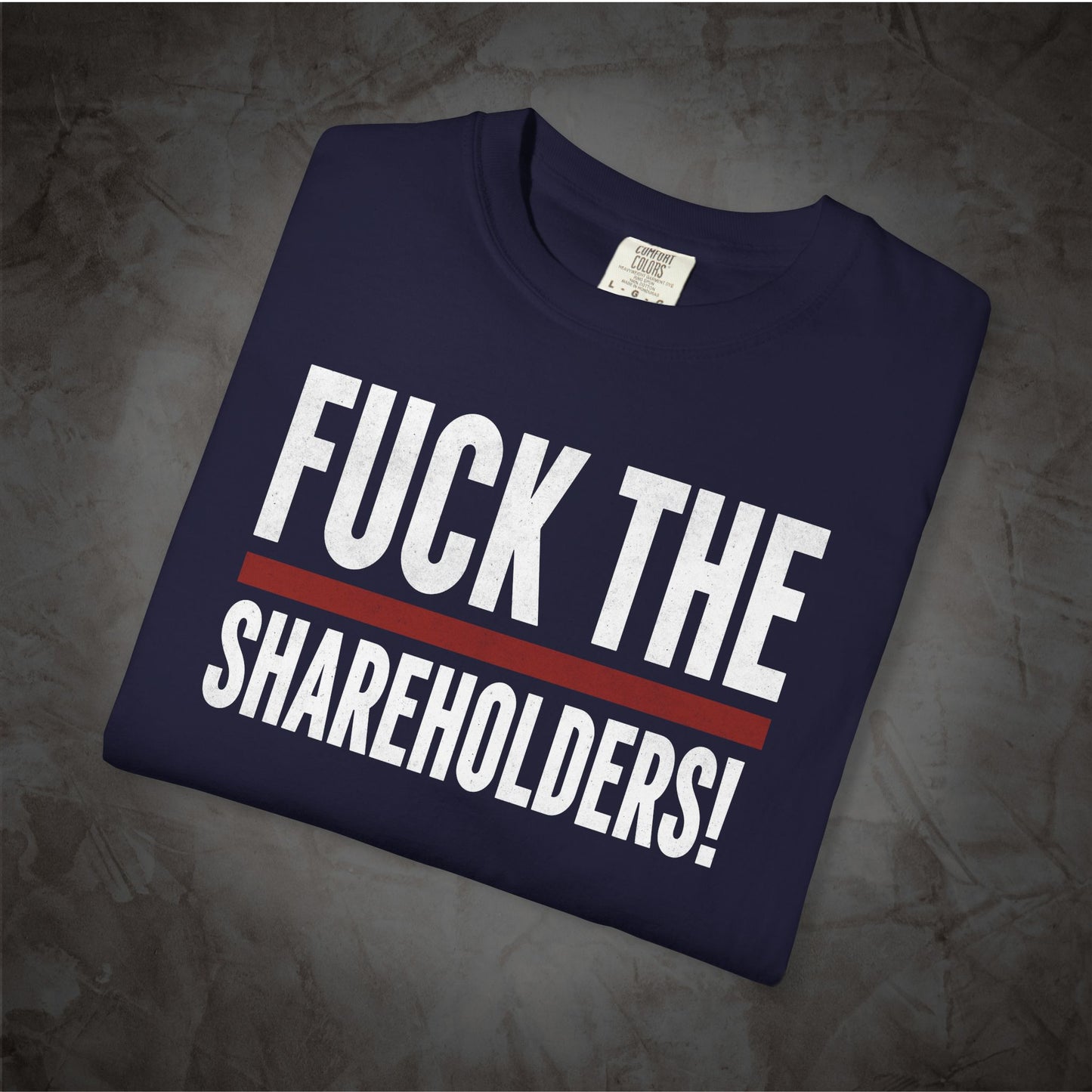 A navy blue folded t-shirt with the text 'FUCK THE SHAREHOLDERS!' printed in bold white letters and a red horizontal stripe, displayed on a textured gray background.