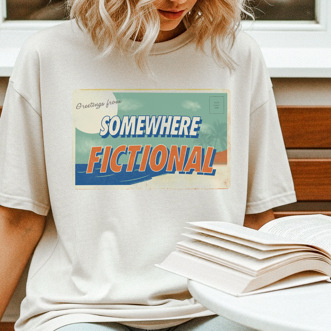Close-up of a person reading books while wearing an ivory “Greetings from Somewhere Fictional” vintage graphic t-shirt.
