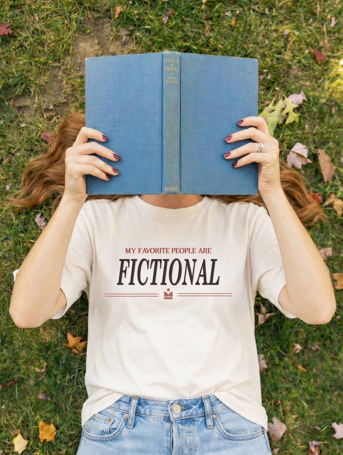 Person wearing a 'Bibliotherapy' t-shirt, lying on grass with a blue book covering their face.
