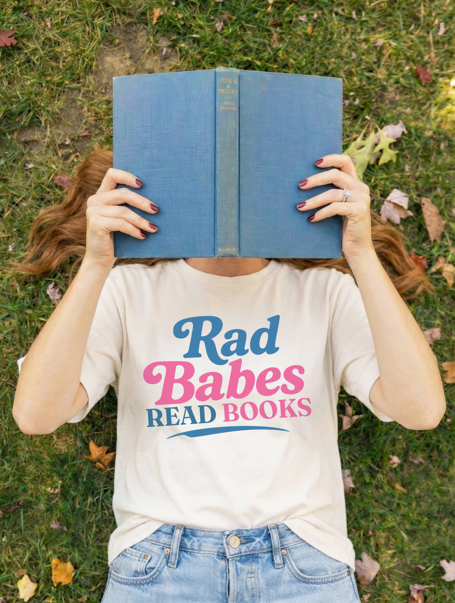 2. Lifestyle Mockup
    Person wearing the Rad Babes Read Books graphic t-shirt while holding a blue book.