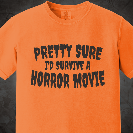 An orange short-sleeve t-shirt with the phrase 'PRETTY SURE I'D SURVIVE A HORROR MOVIE' printed in a black, distressed font across the chest, displayed against a dark textured background.