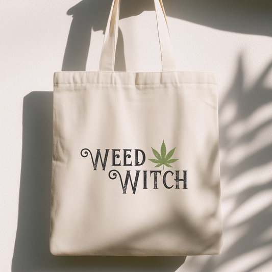 A cream-colored canvas tote bag with the words 'WEED WITCH' printed in a dark gray gothic font, accented by a green cannabis leaf. The bag is photographed hanging against a white wall with dramatic shadows cast across it.