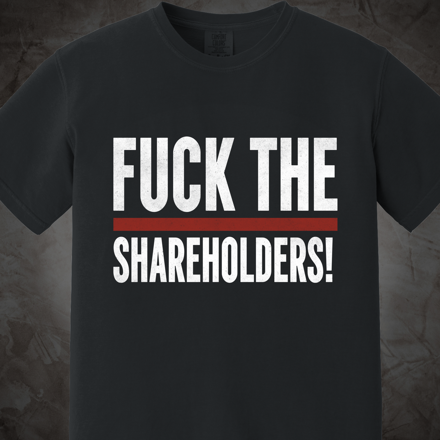 A dark charcoal gray crewneck t-shirt featuring the text 'FUCK THE SHAREHOLDERS!' printed in distressed white capital letters, separated by a single horizontal red stripe.