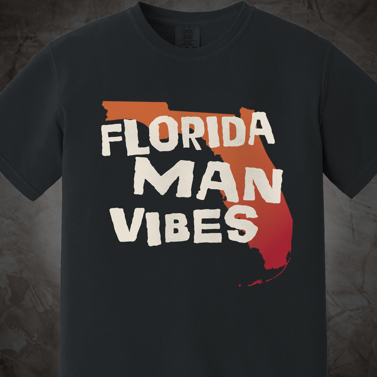 A dark charcoal gray t-shirt featuring a graphic of the state outline of Florida filled with a red-orange gradient and the text 'FLORIDA MAN VIBES' in a distressed white font.
