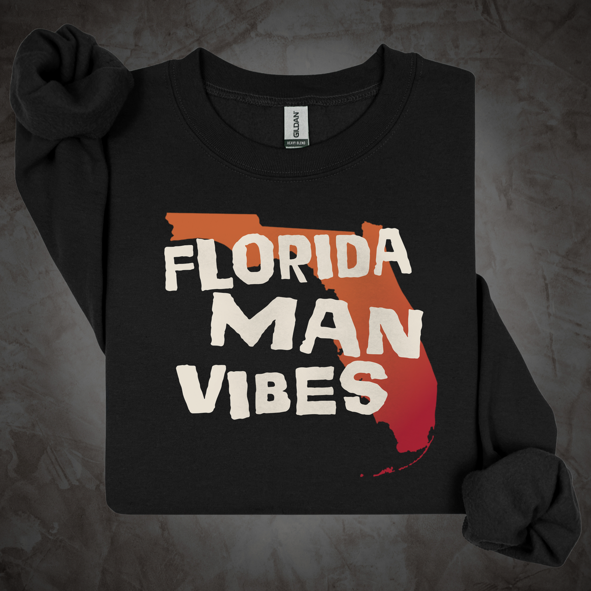 A black long-sleeve t-shirt with rolled cuffs, featuring a graphic print of the state of Florida filled with a red-to-orange gradient and the text 'FLORIDA MAN VIBES' in white. The shirt is laid flat on a textured gray background.