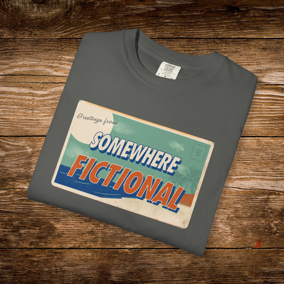 Folded Pepper Comfort Colors t-shirt with the “Greetings from Somewhere Fictional” retro graphic.