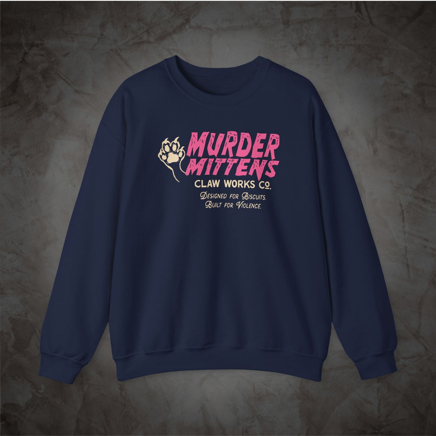 A navy blue crewneck sweatshirt with a graphic on the chest reading 'MURDER MITTENS CLAN WORKS CO' in pink and white, featuring a clenched fist illustration, displayed on a textured gray background.