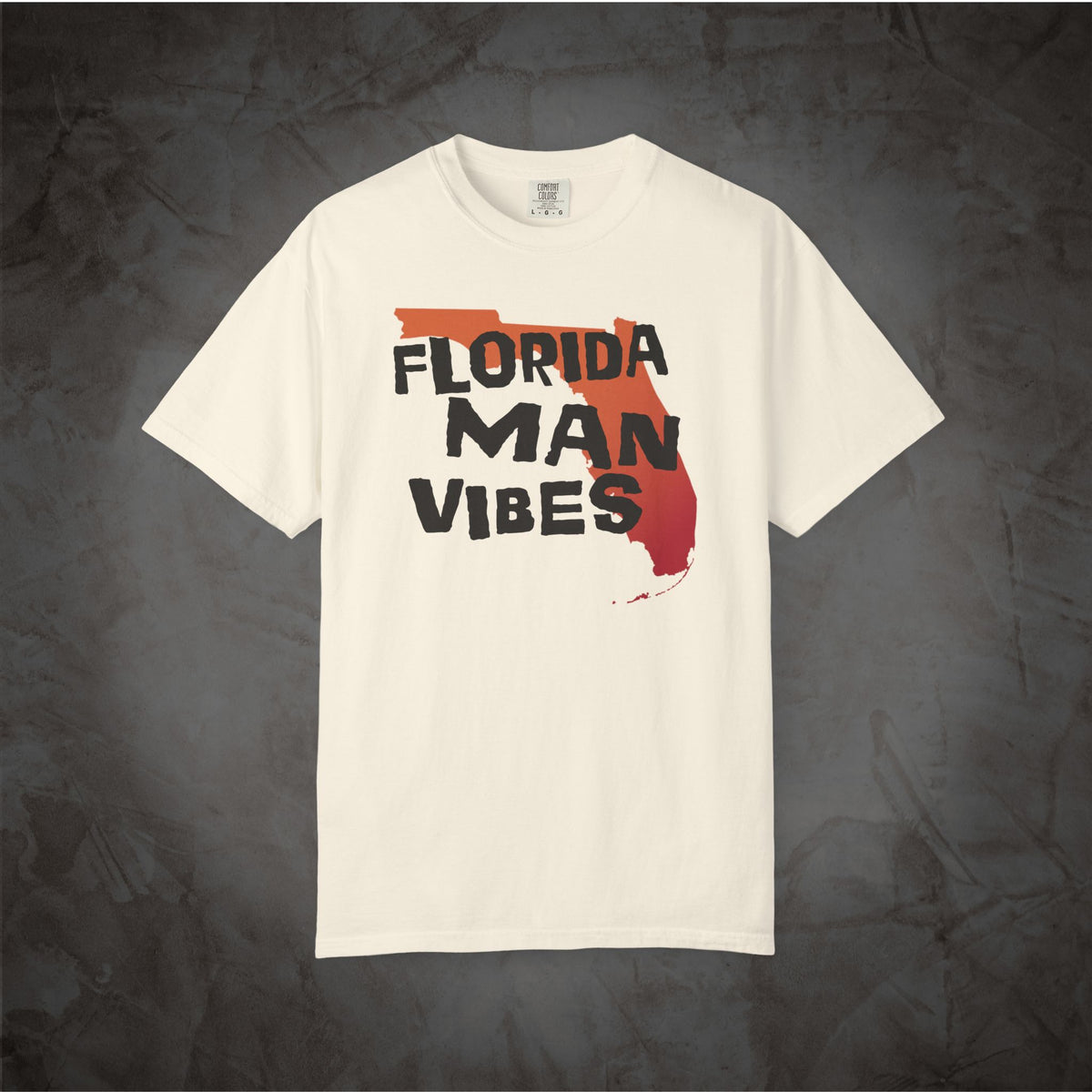 An off-white short-sleeve t-shirt with a graphic print on the front. The graphic features the text 'FLORIDA MAN VIBES' in black lettering over a red and orange silhouette of the state of Florida.