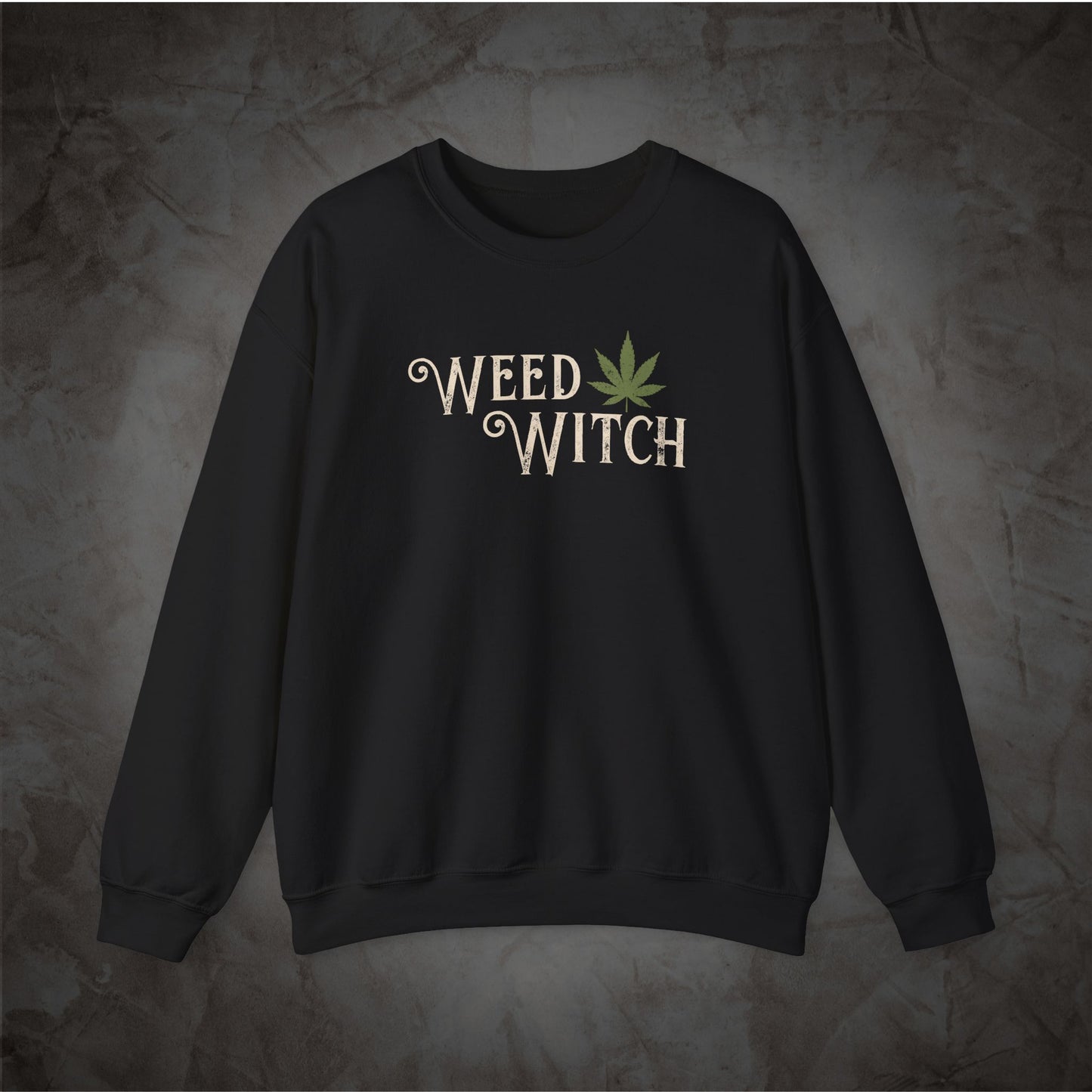 A black crewneck sweatshirt featuring the words 'WEED WITCH' in a distressed cream font with a green cannabis leaf graphic, displayed against a textured dark gray background.
