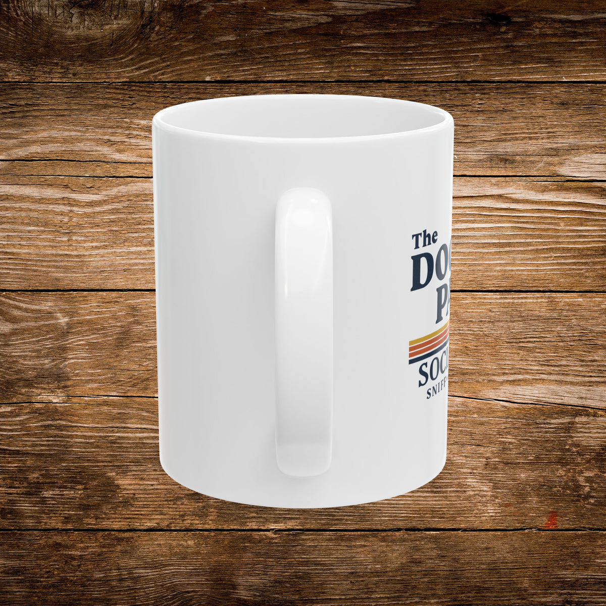 A white ceramic coffee mug with a printed graphic on the side, displayed on a rustic brown wooden plank background. The graphic features the text 'The DOG PUP' and 'SOCIAL' in dark blue lettering with a retro orange and yellow stripe design.