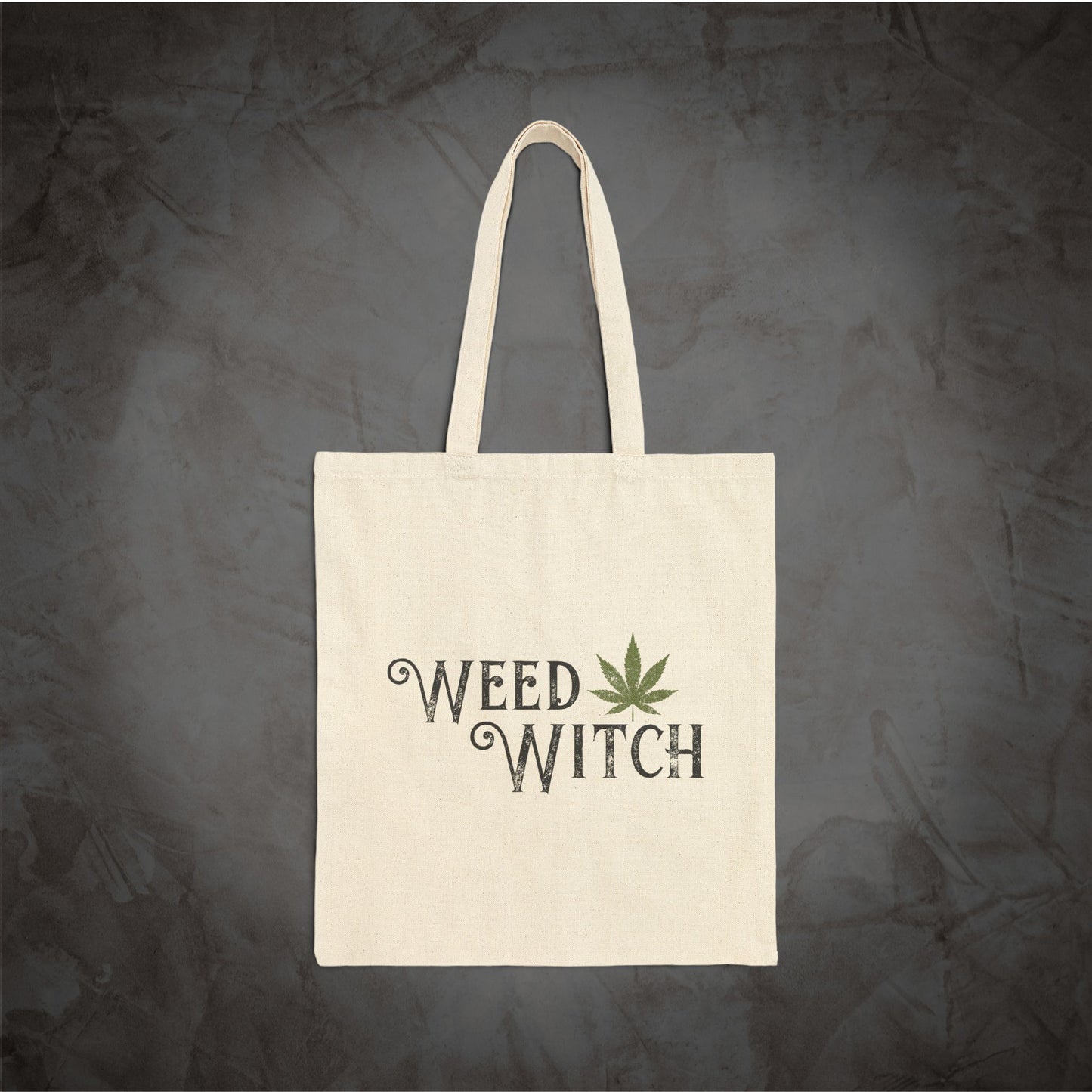 An off-white canvas tote bag with two handles, featuring the words 'WEED WITCH' in a dark gray gothic font and a green cannabis leaf graphic, set against a dark textured gray background.