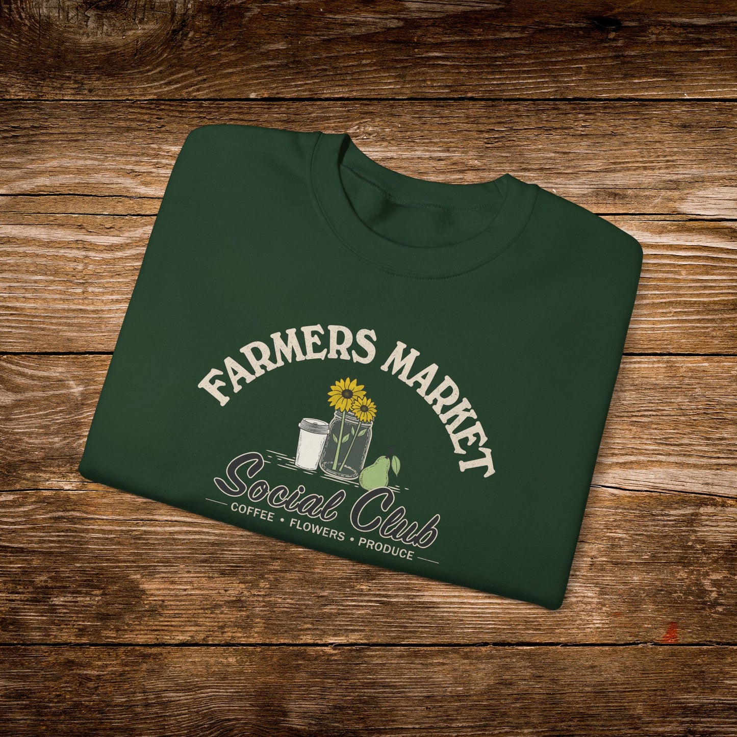 A dark green folded t-shirt with a 'Farmers Market Social Club' graphic, displayed flat on a rustic wooden background.