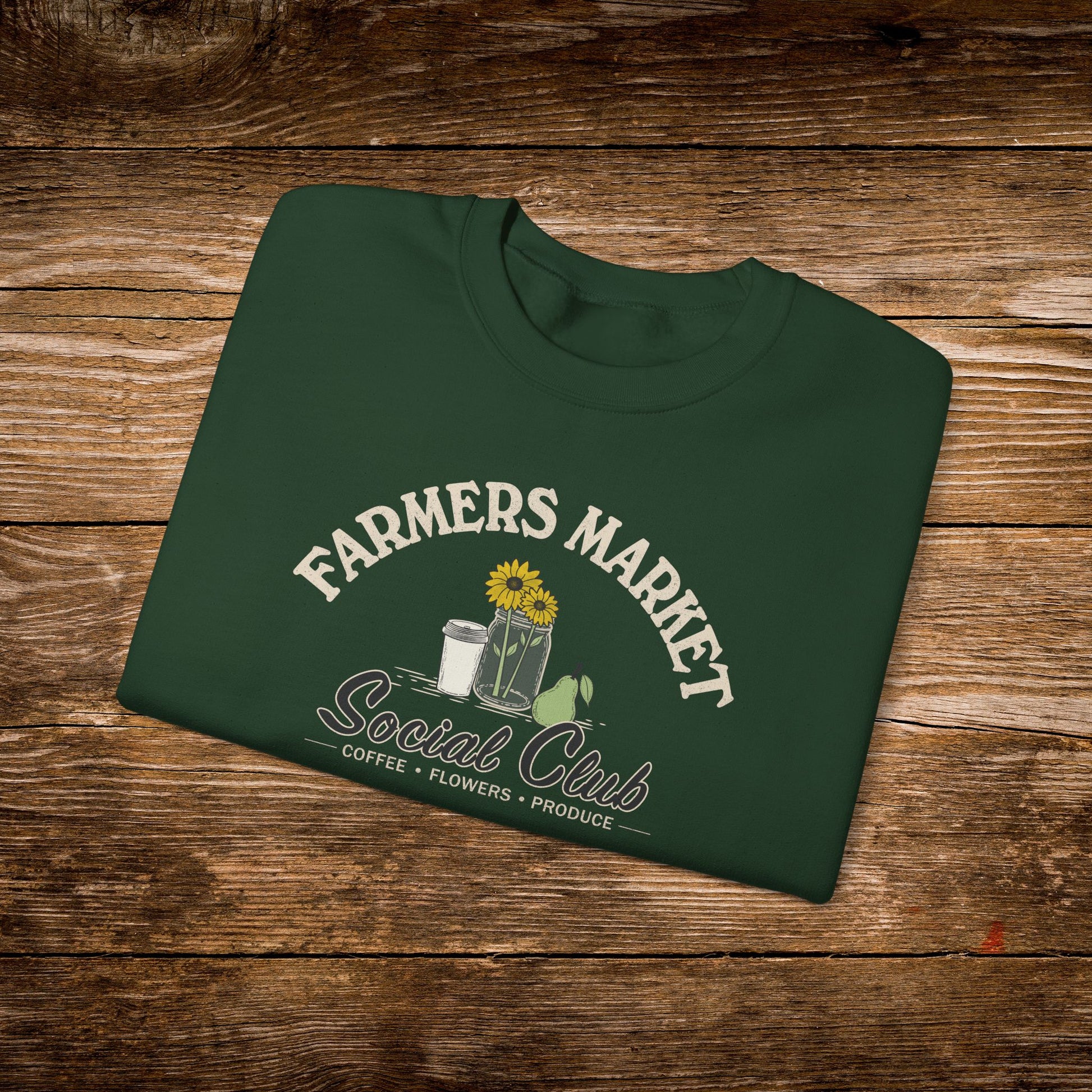 A dark green folded t-shirt with a 'Farmers Market Social Club' graphic, displayed flat on a rustic wooden background.