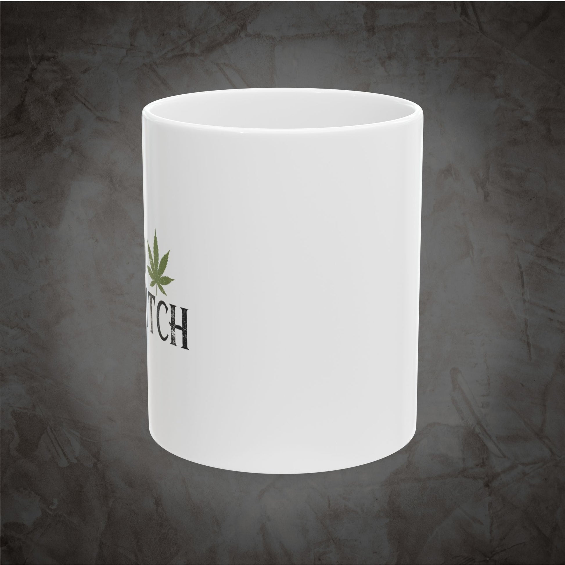 A white ceramic mug with a green cannabis leaf graphic and the partial black text 'TCH' printed on the side, shown against a dark textured gray background.