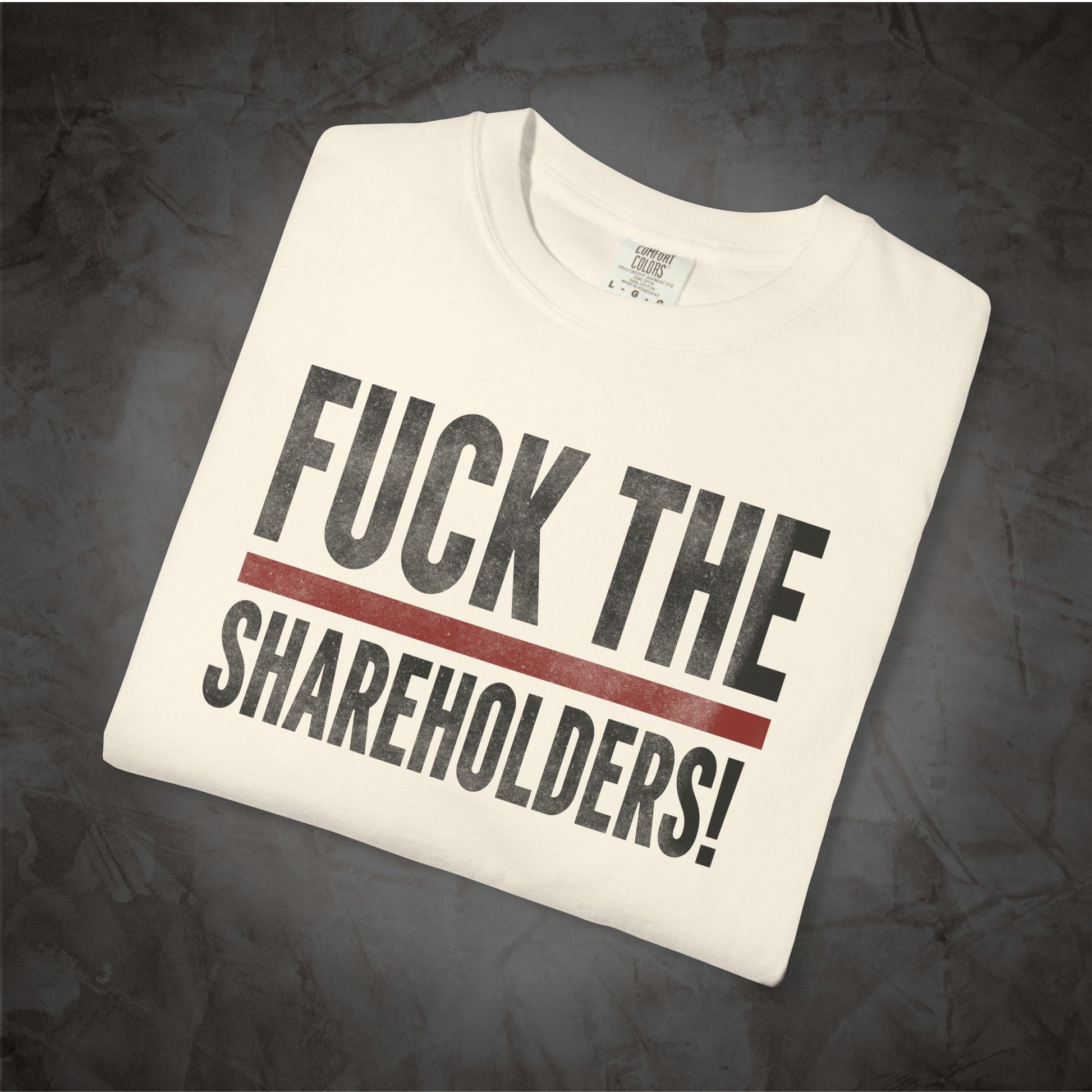 A white crewneck t-shirt with the text 'FUCK THE SHAREHOLDERS!' printed in black, separated by a thick red horizontal line, displayed on a dark textured background.