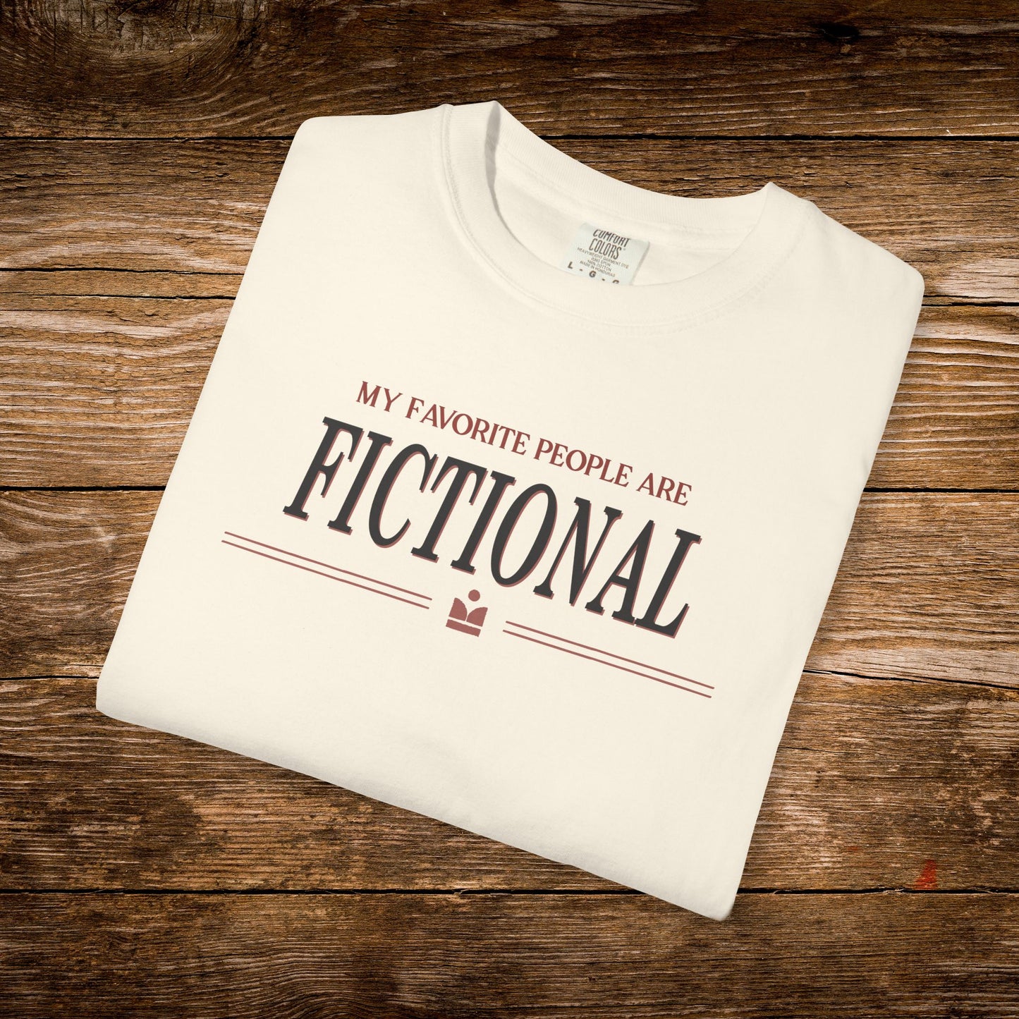 Folded white t-shirt with text 'My favorite people are fictional' on a wooden surface