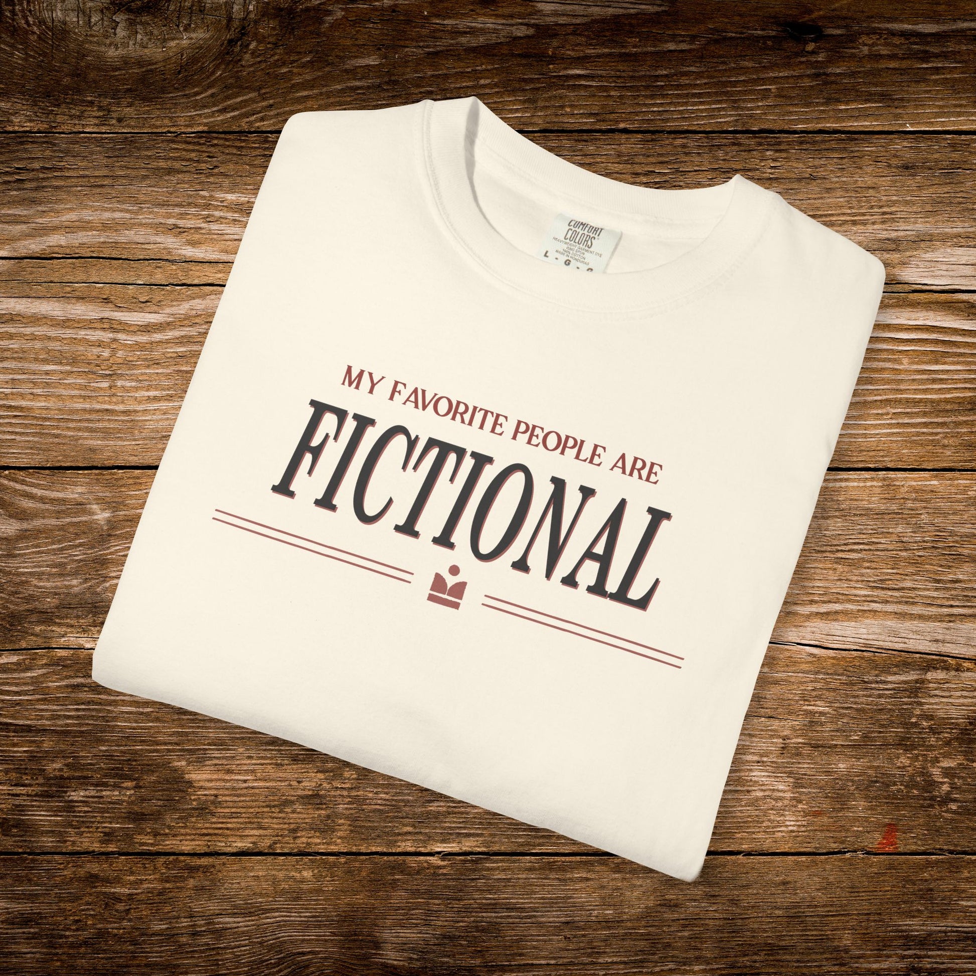 Folded white t-shirt with text 'My favorite people are fictional' on a wooden surface