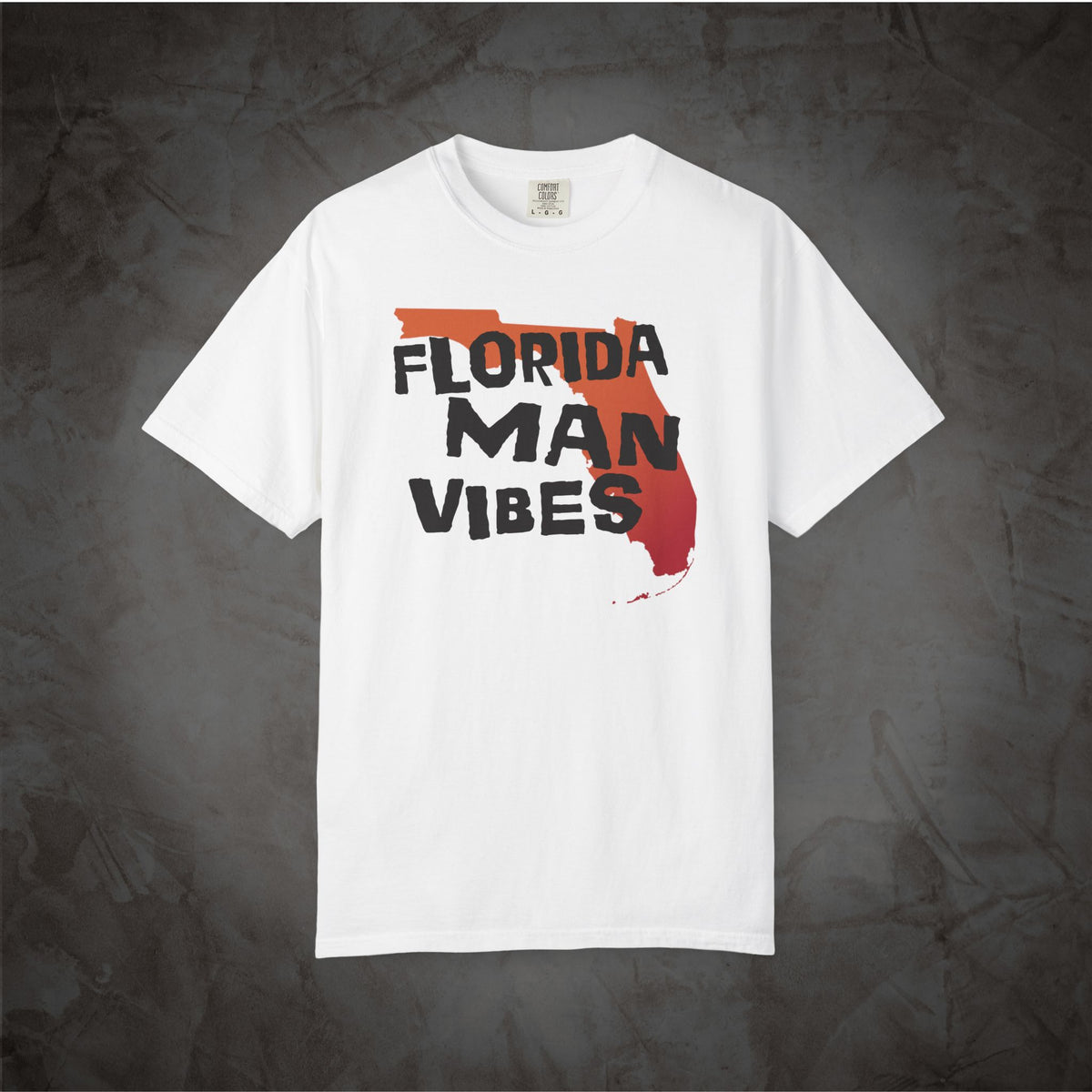 An off-white short-sleeve t-shirt with a graphic print on the front. The graphic features the text 'FLORIDA MAN VIBES' in black lettering over a red and orange silhouette of the state of Florida.