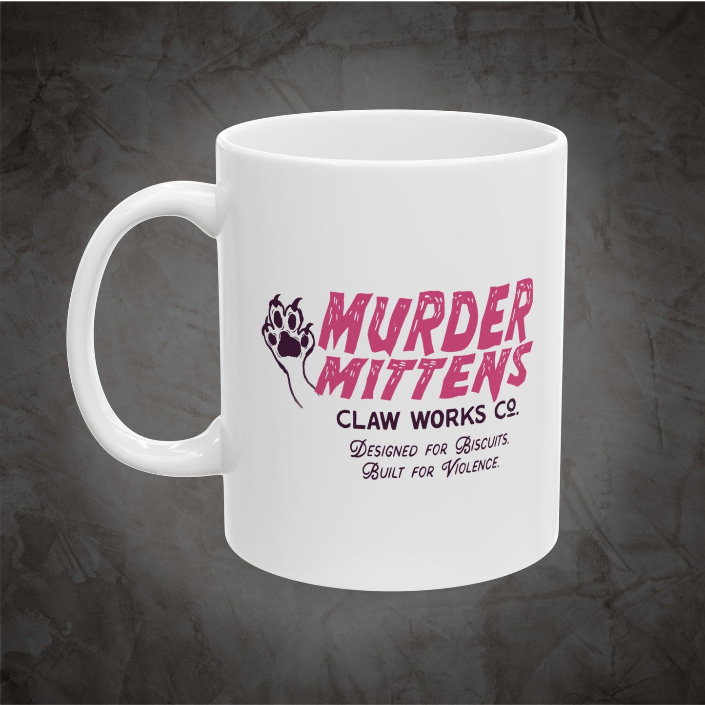 A white ceramic mug featuring a pink and black graphic print that reads 'MURDER MITTENS CLAW WORKS CO.' with a paw print and the tagline 'Designed for Biscuits.
