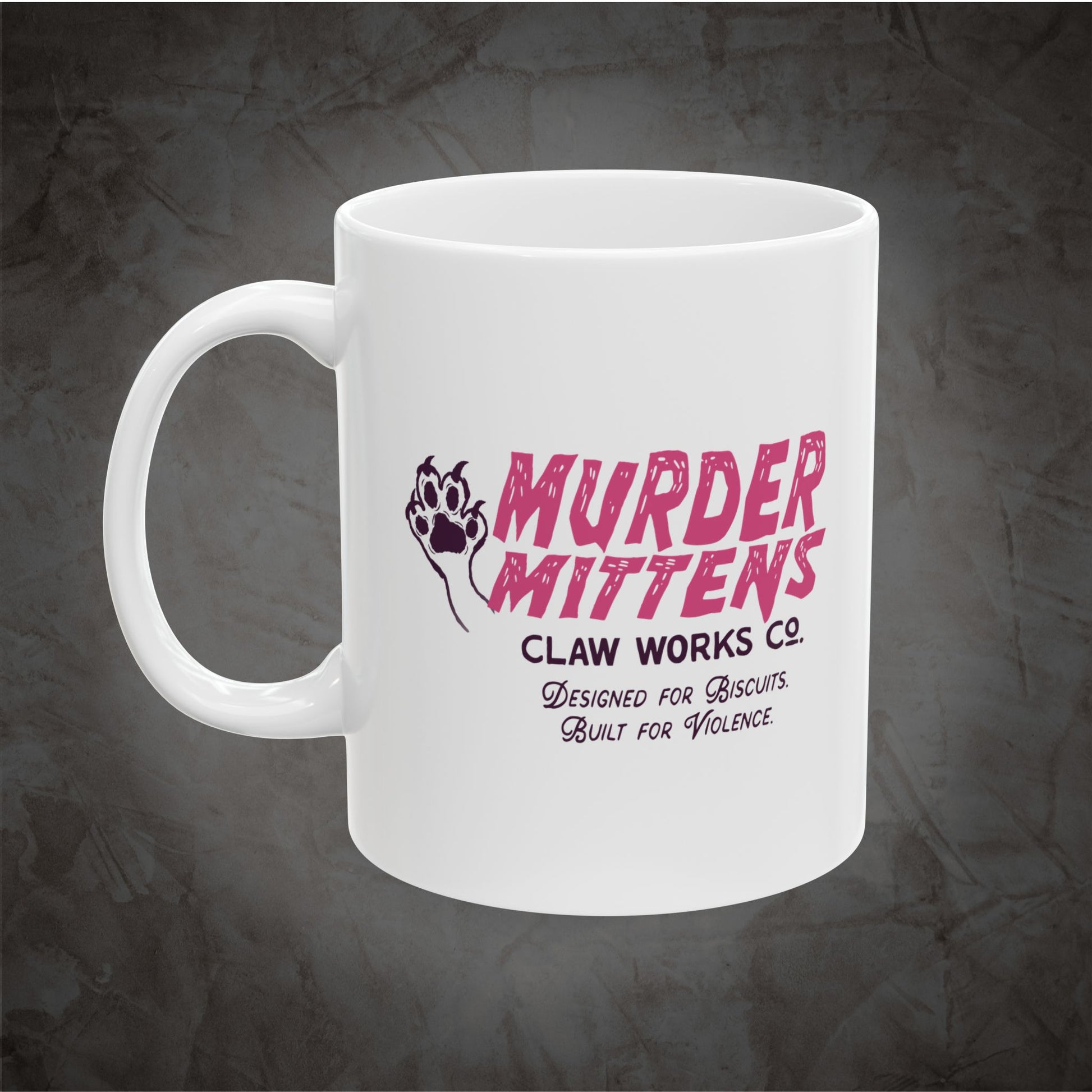 A white ceramic mug featuring a pink and black graphic print that reads 'MURDER MITTENS CLAW WORKS CO.' with a paw print and the tagline 'Designed for Biscuits.
