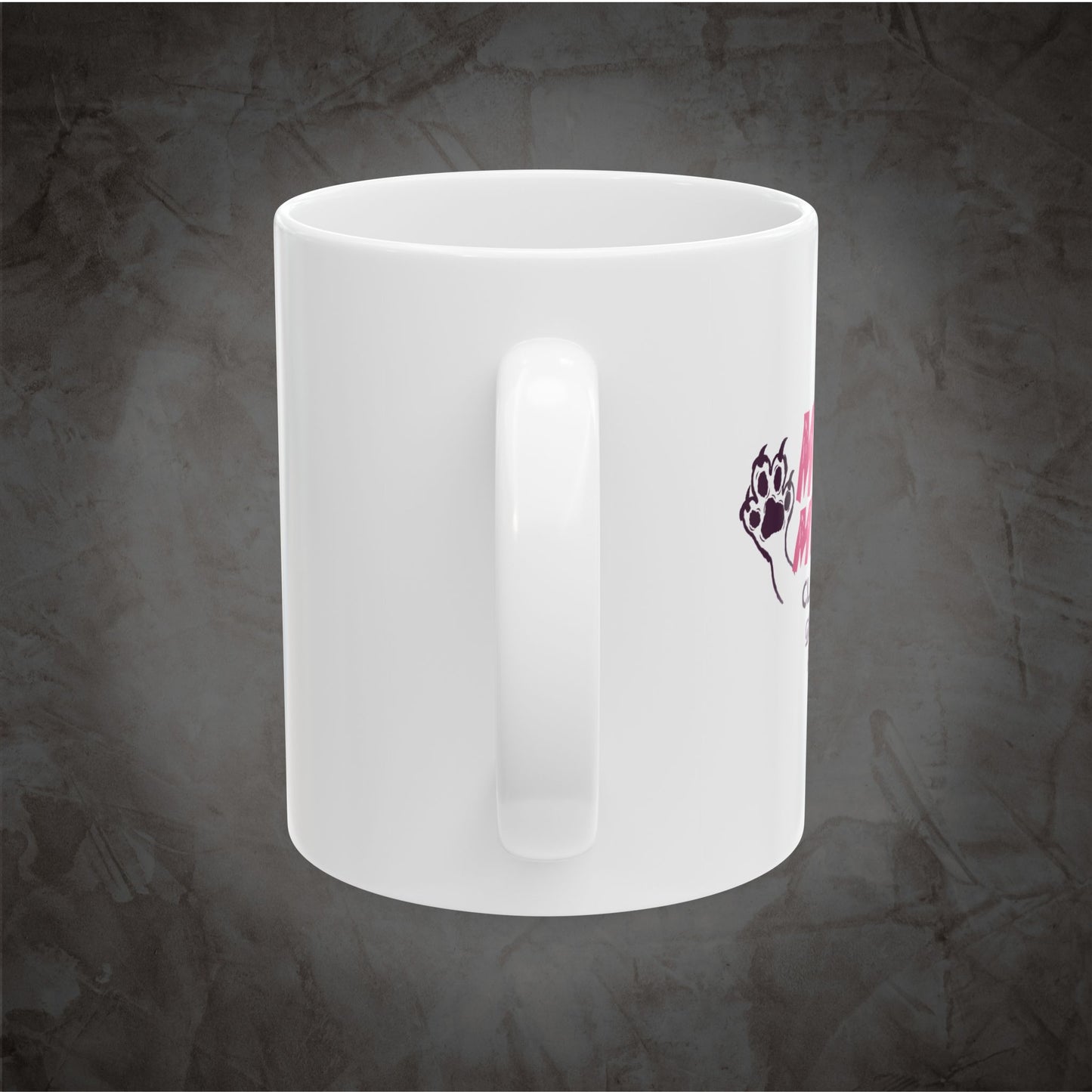 A white ceramic coffee mug with a handle, featuring a small graphic of a black paw print with pink hearts on the side, set against a textured dark gray background.