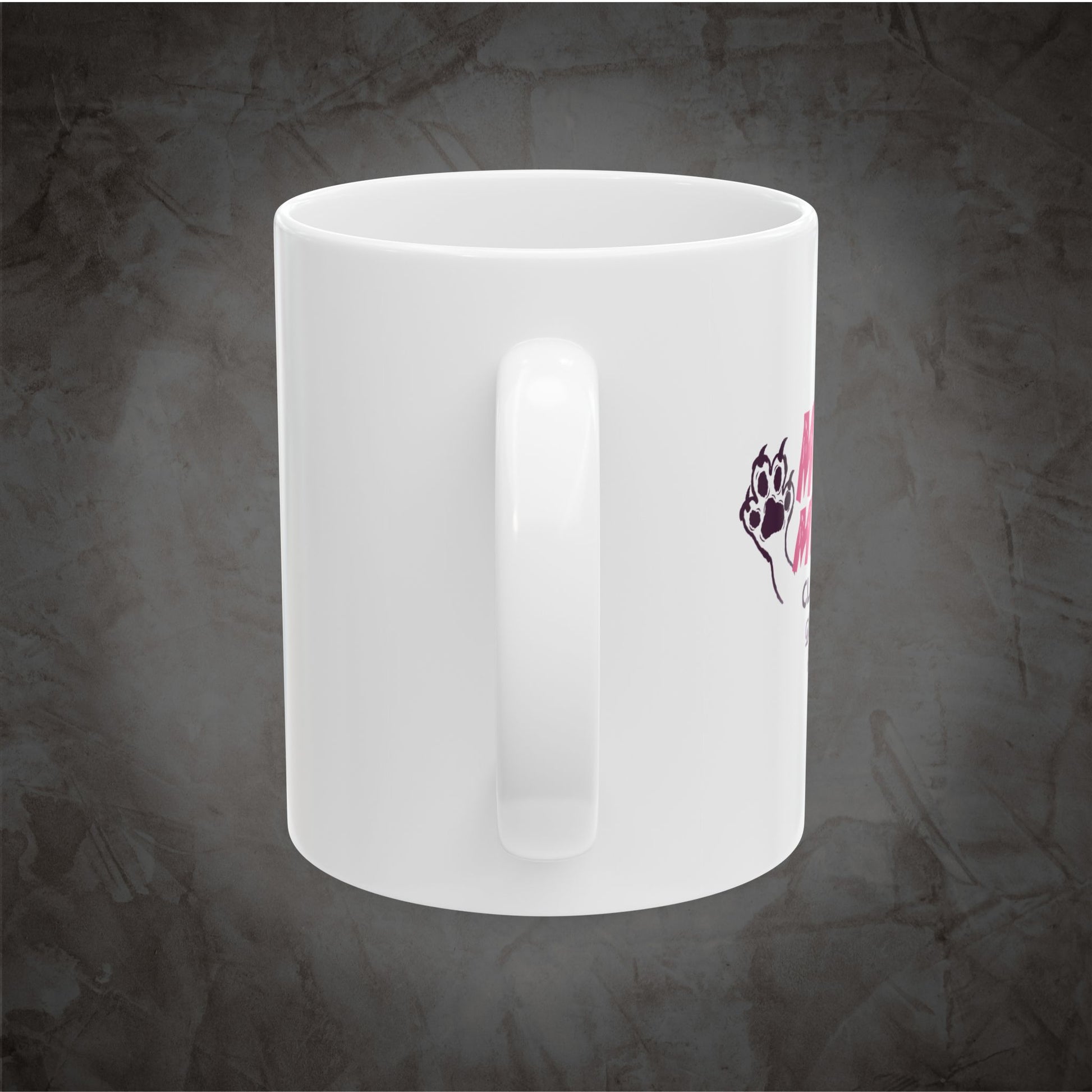 A white ceramic coffee mug with a handle, featuring a small graphic of a black paw print with pink hearts on the side, set against a textured dark gray background.